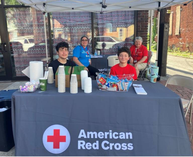 group of people sitting at table with red cross tablecloth