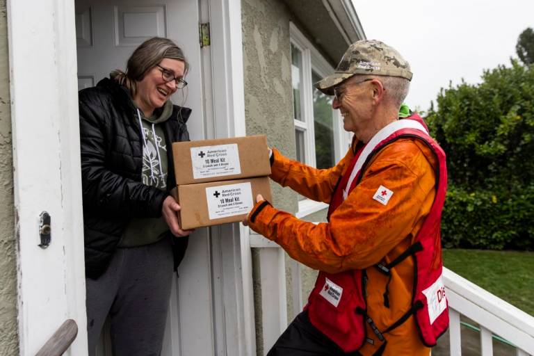man in Red Cross vest delivers boxes to woman at her front door