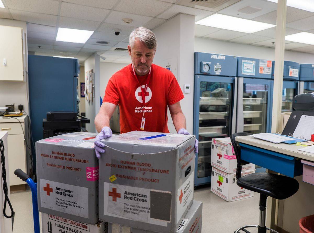 man in Red Cross shirt in blood distribution center getting order of boxes of blood products ready to deliver to hospitals