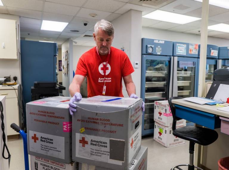 man in Red Cross shirt in blood distribution center getting order of boxes of blood products ready to deliver to hospitals.