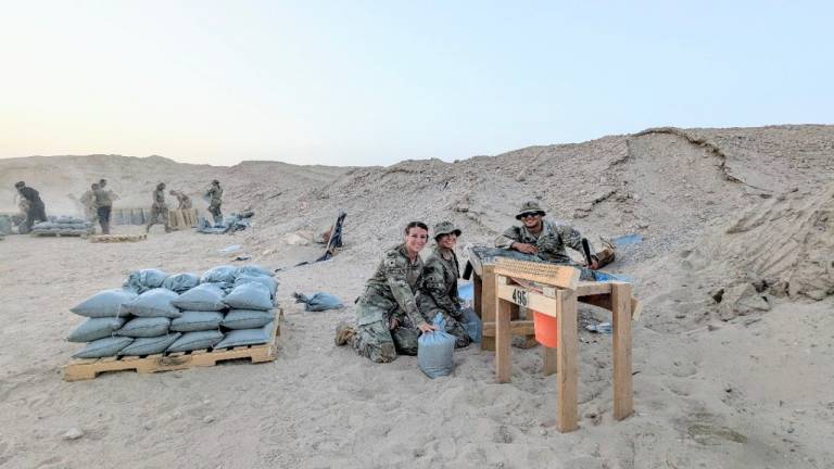 Active-duty service members kneel beside a pallet of sandbags which they filled for the base as Red Cross volunteers.
