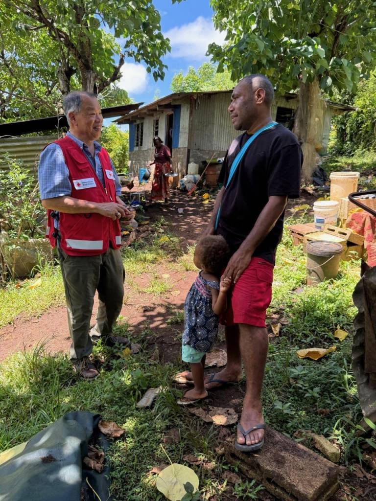 Two men and a child stand in the sunshine speaking to one another. 