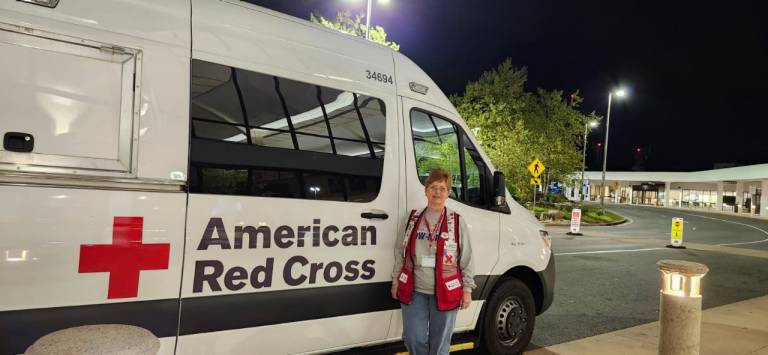 woman in Red Cross vest stands in front of Red Cross vehicle