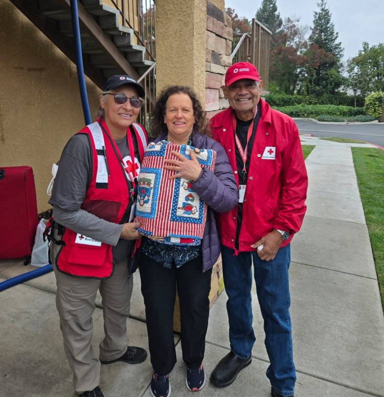 Two Red Cross volunteers hand a quilt to a woman affected by a home fire.