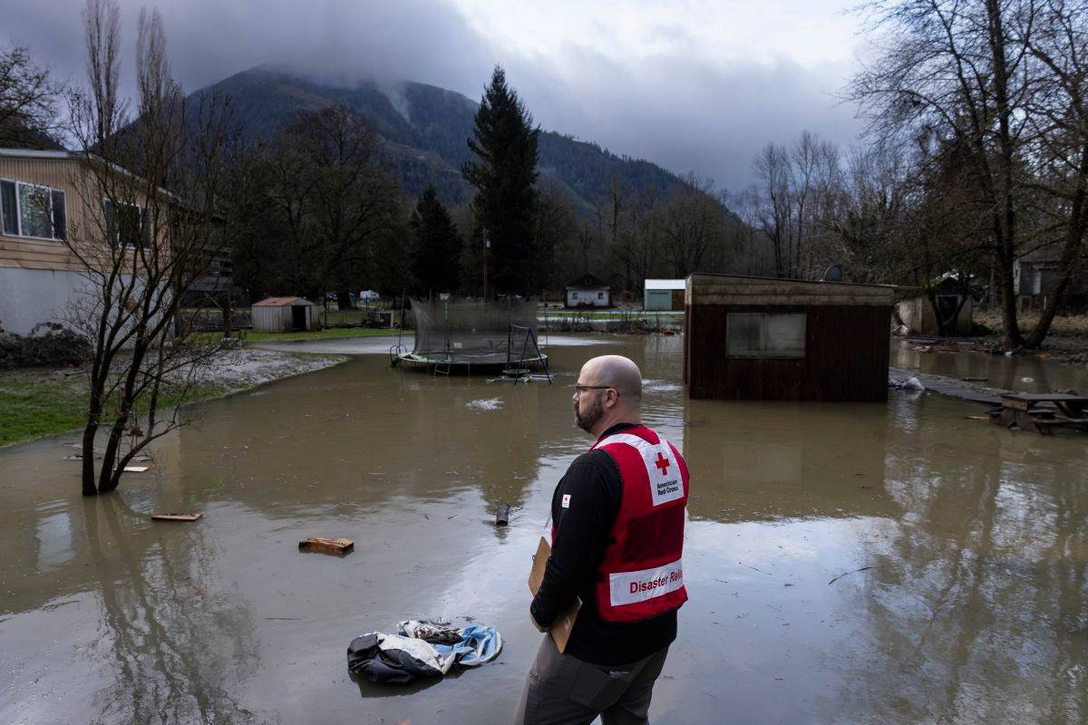 Man in Red Cross vest looks out over floodwater.
