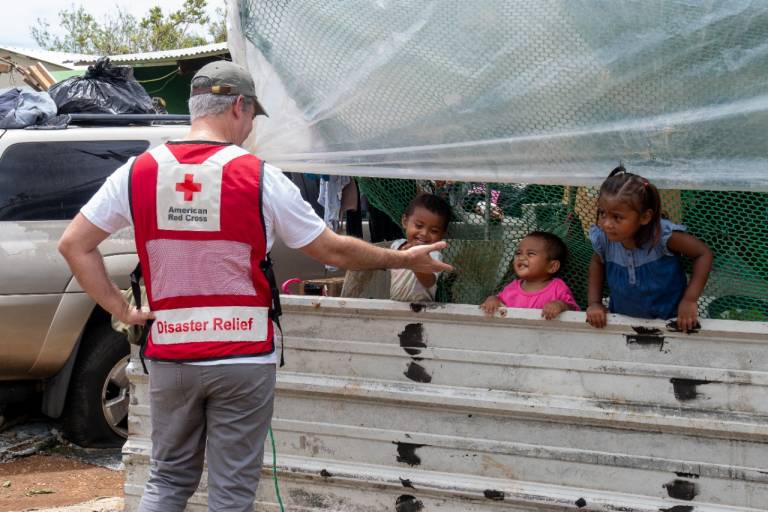 Man in Red Cross vest amuses three small children. 