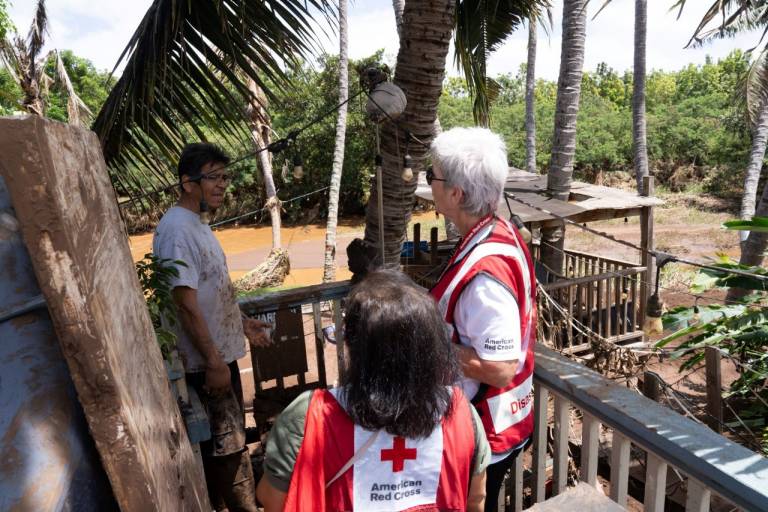 Two people in Red Cross vests talk with a man on his deck