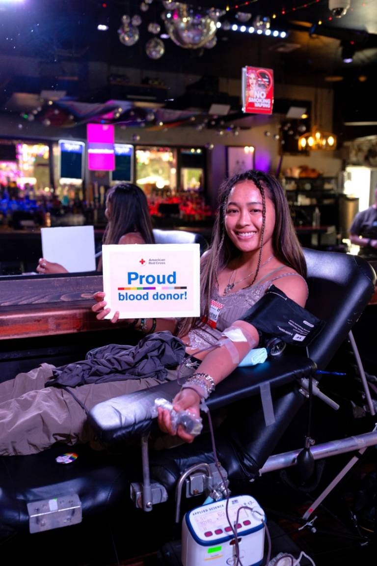 A smiling woman giving blood at a Gossip Grill blood drive.