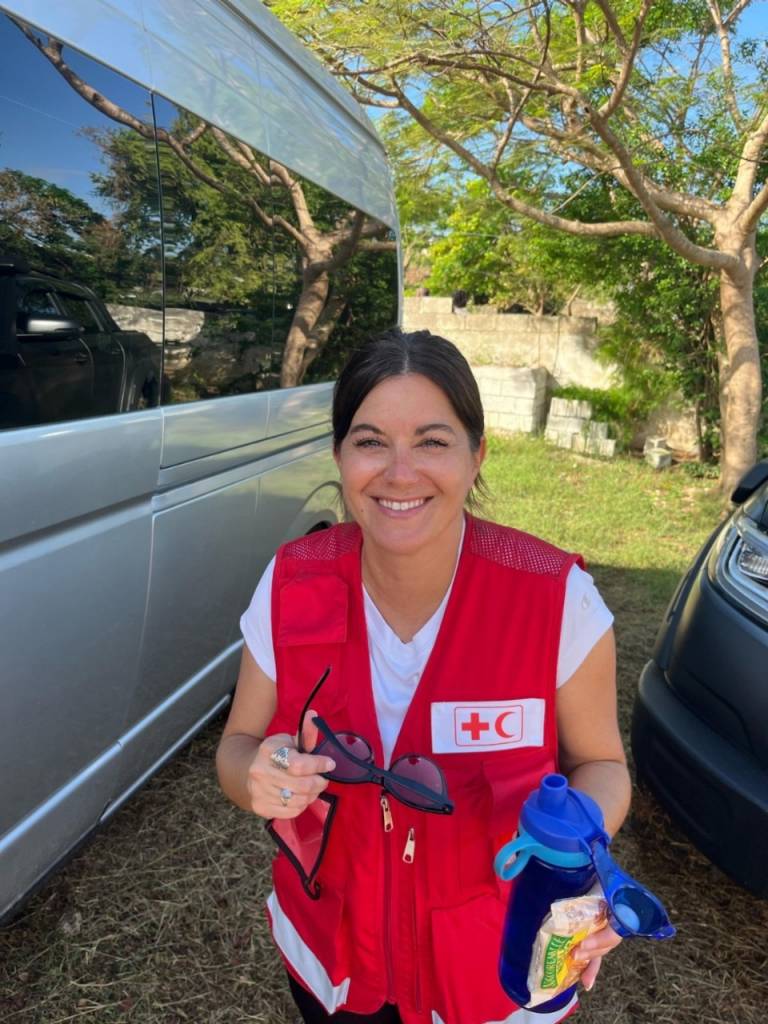 A woman in a red vest stands smiling in front of a van. 