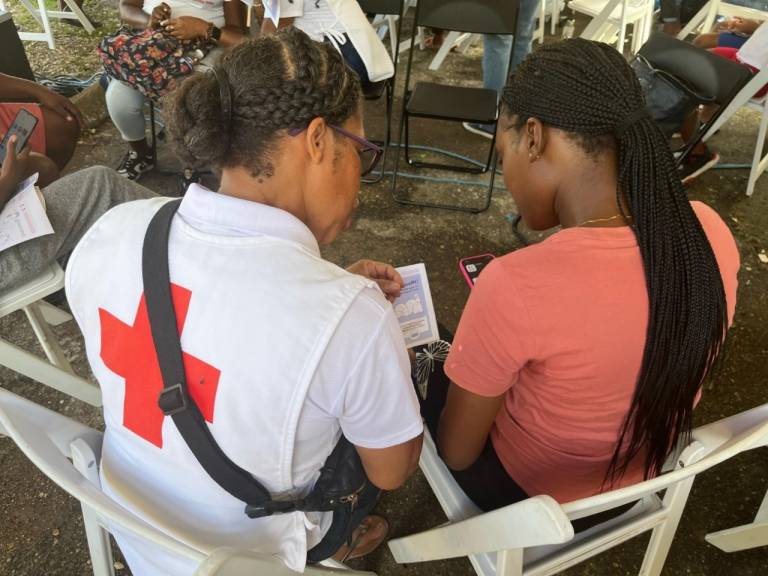 A Red Cross worker and a community member in a pink shirt sit with their backs to the camera while filing Red Cross assistance paperwork. 