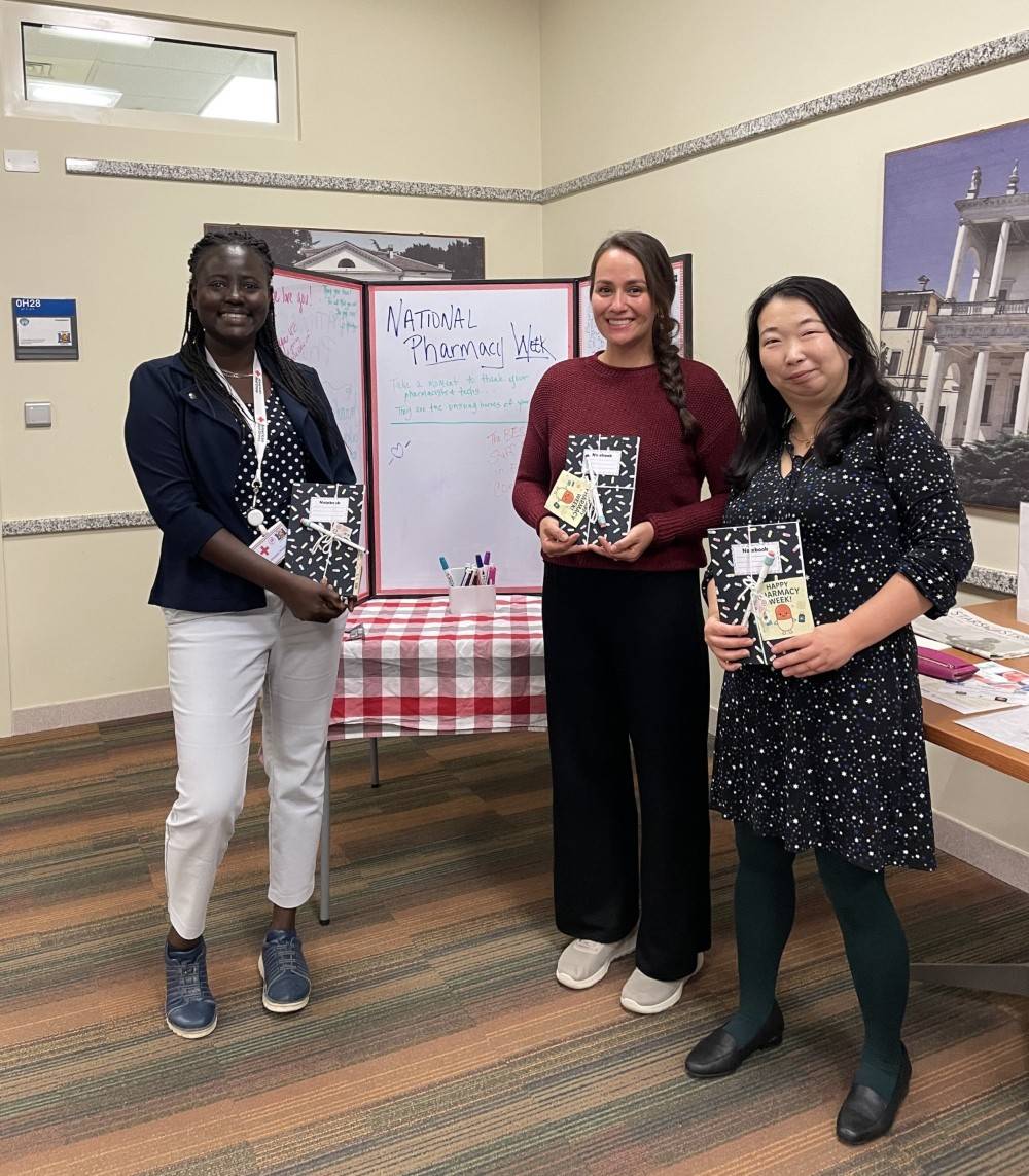 A group of three women stand in front of a table holding notebooks and smiling.