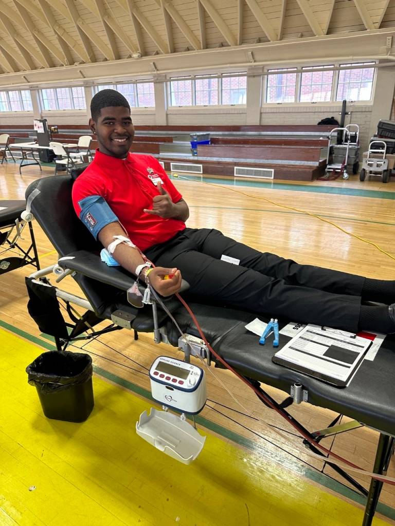 Michael C. Prescot, Jr. donating whole blood while seated in a donation chair at a campus blood drive.