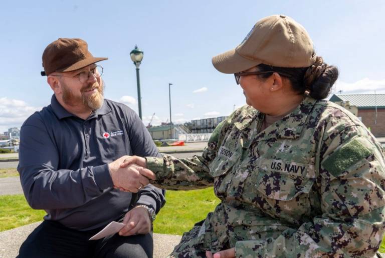 Man in Red Cross shirt sits and talks to woman in military uniform