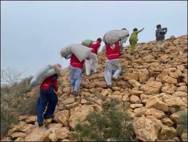 People in Red Crescent vests help people evacuate up a steep hillside