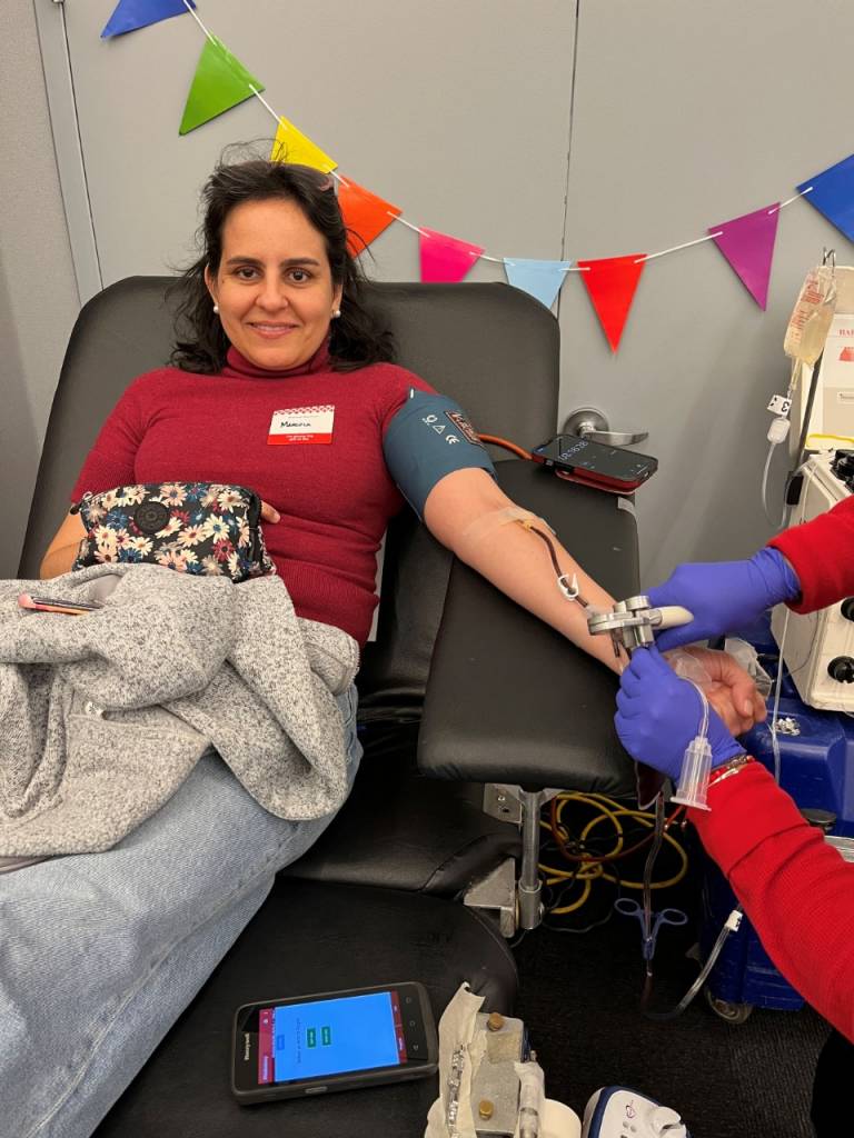Woman in red shirt on blood donor bed giving blood