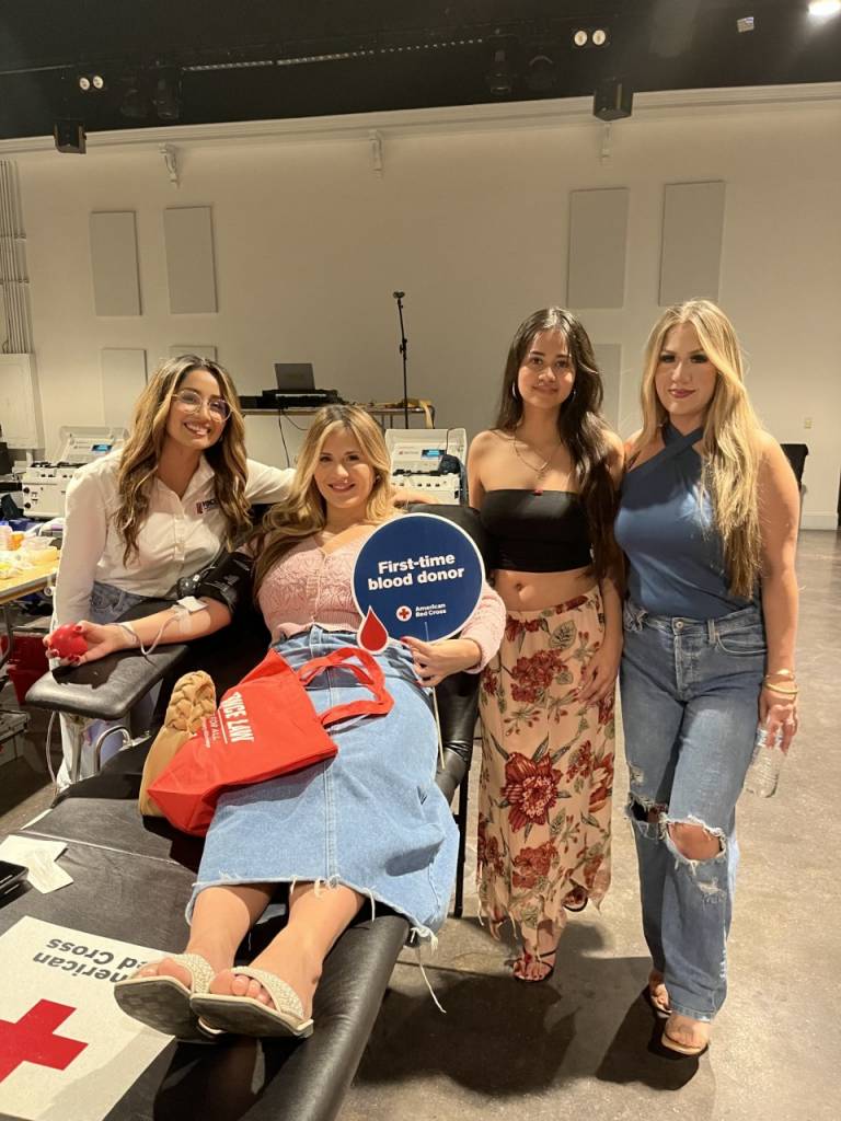 Four women, one on a blood donor bed, stand in a Red Cross blood donation facility.
