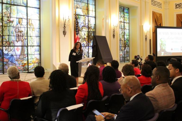 Woman stands behind a podium addressing roomful of people