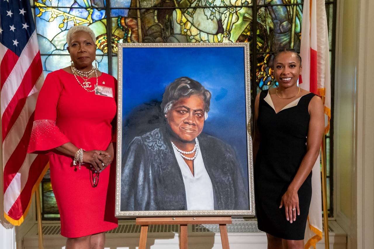 Two women stand with portrait  of Dr. Bethune