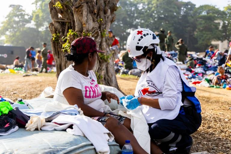 A Red Cross medical worker assesses a resident affected by the earthquake under a tree. 