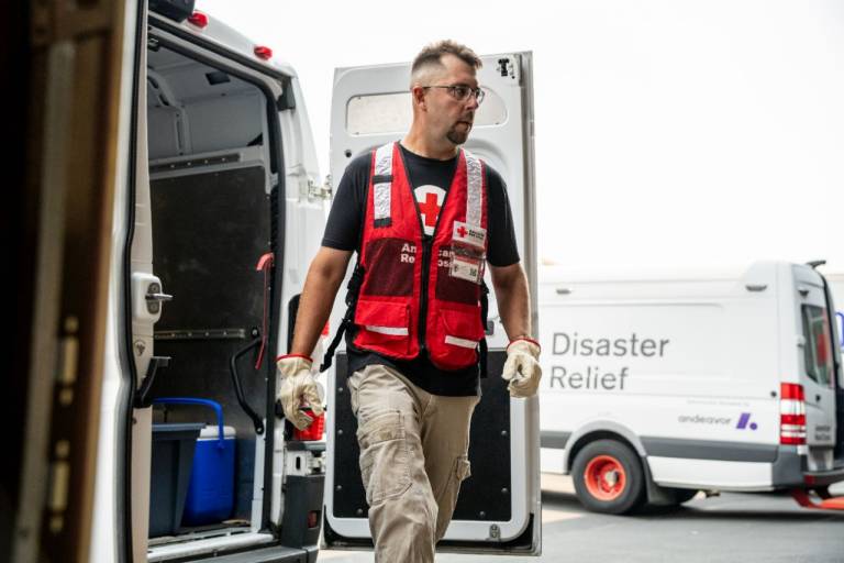 Man in Red Cross vest loads supplies into a Red Cross vehicle.