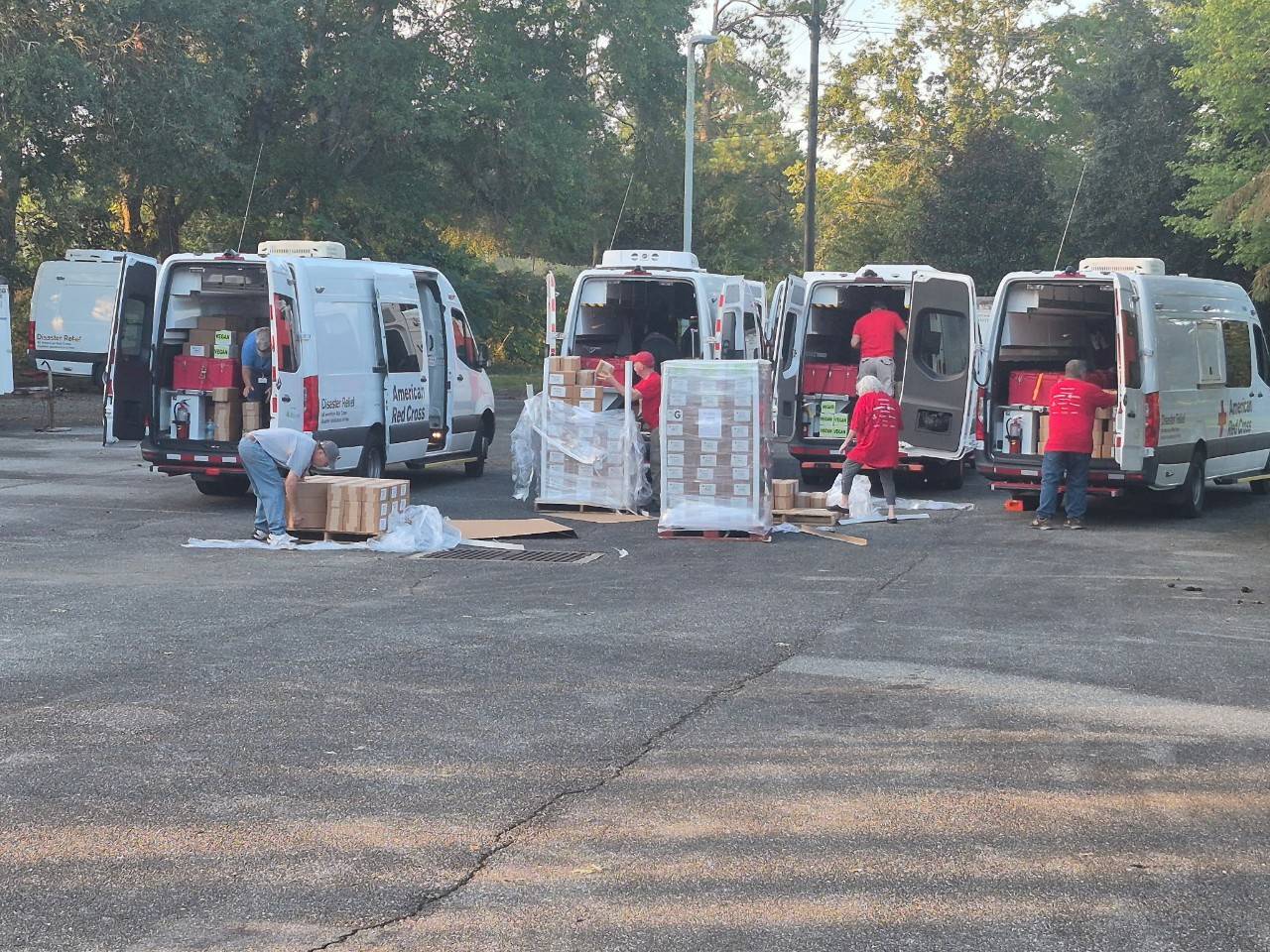 People in Red Cross shirts load supplies into a line of emergency vehicles.