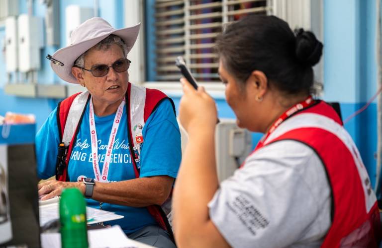 Two women in Red Cross vests sit outside at a table talking
