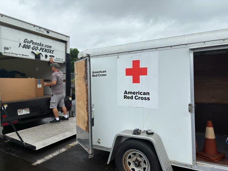 Man in gray Red Cross tee shirt closes the back of a large truck.