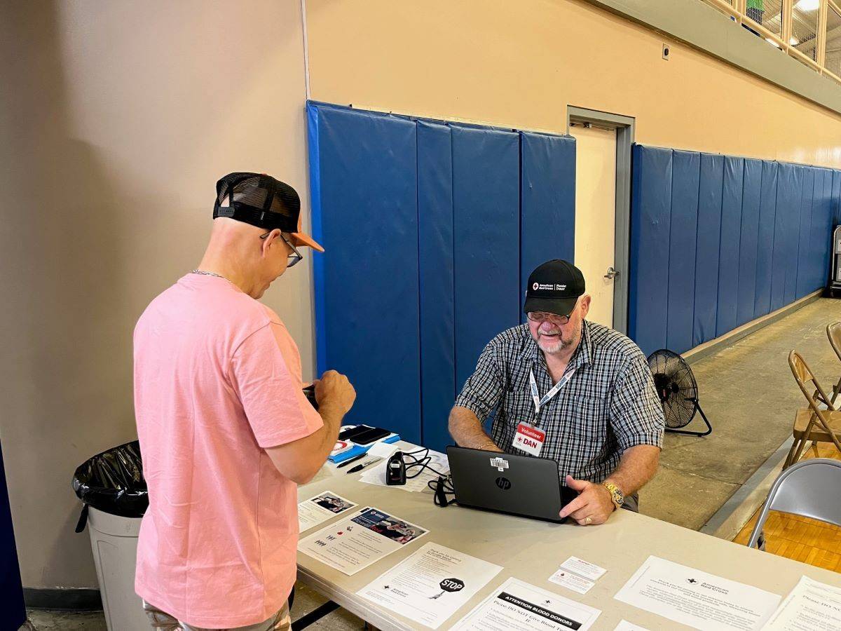 man in Red Cross badge sits at table while man in pink shirt stands