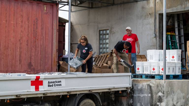 wo men and a woman, all wearing Red Cross shirts, load a truck with relief supplies.