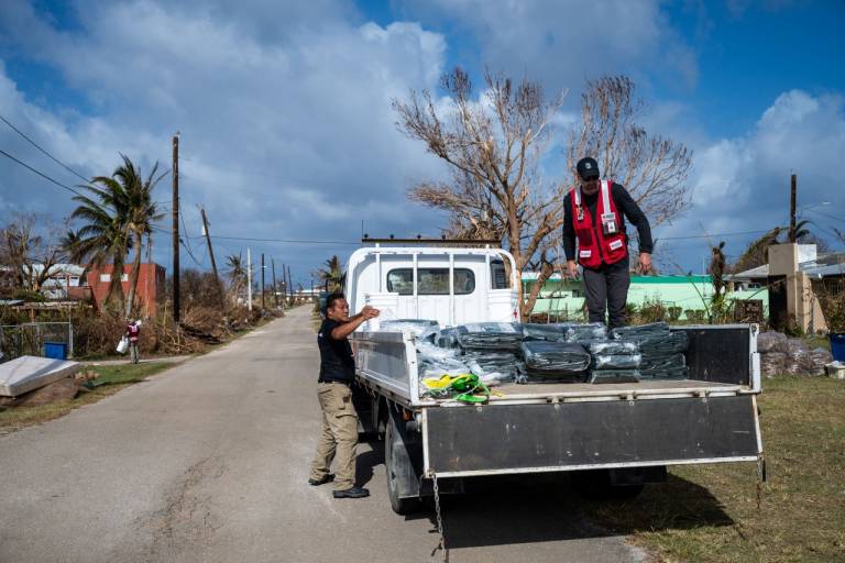Two men in Red Cross shirts work on unloading a truck filled with relief supplies