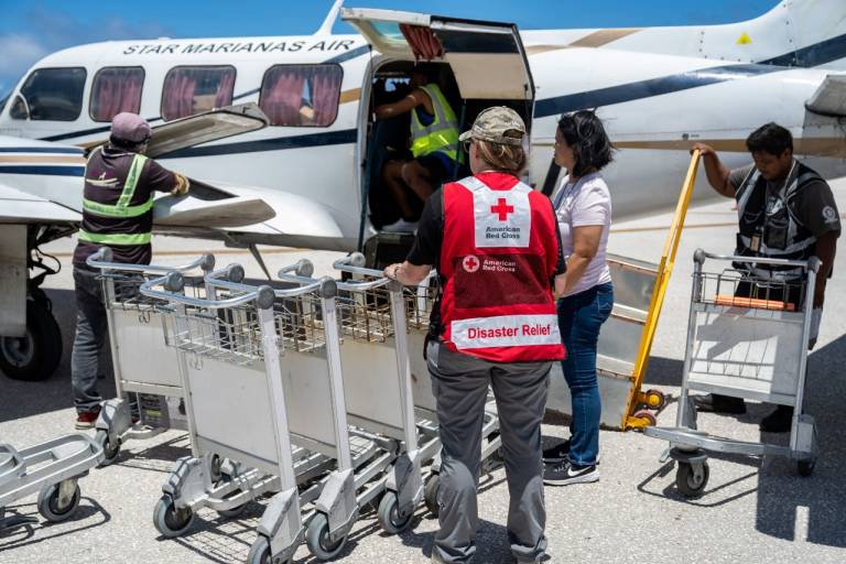 People in Red Cross shirts and vests prepare to unload relief supplies from a plane