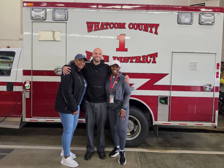 three people stand alongside a firetruck.