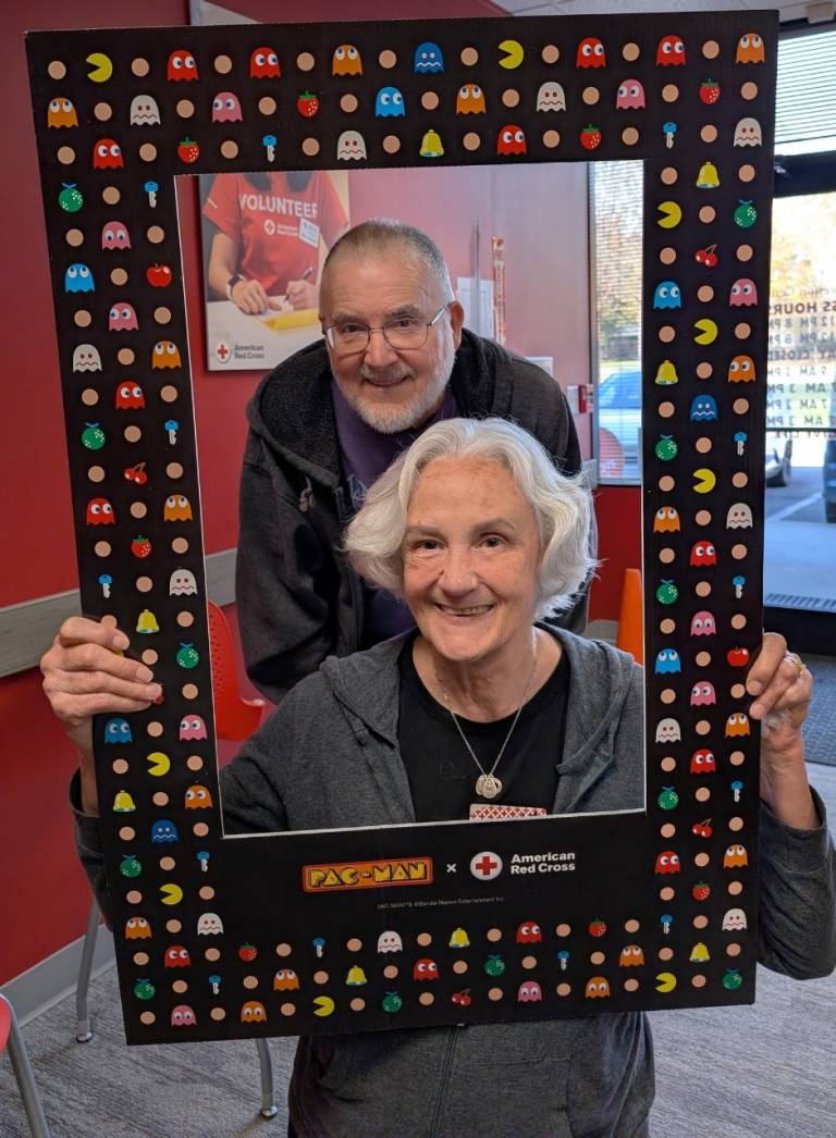 A man and woman pose inside a large Red Cross picture frame.