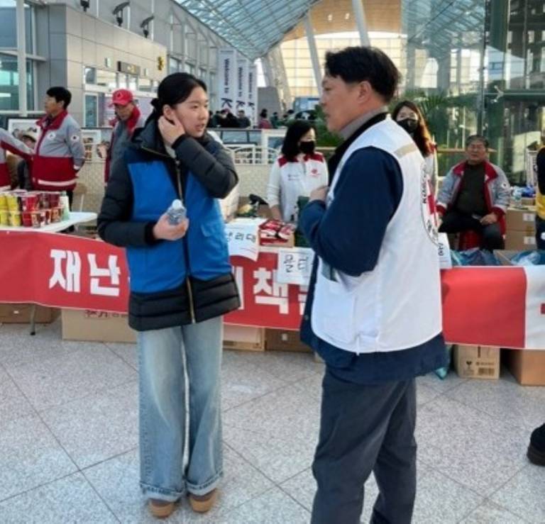 A young woman in a blue jacket talks to a man in a Red Cross vest
