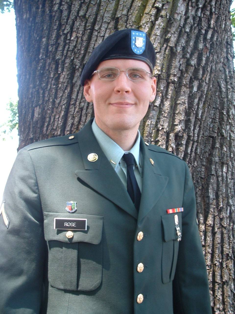Photo of a Spc. Rose from the chest up, wearing an Army service uniform (beret, tie, blazer with brass buttons). He is cleanshaven, wears glasses a few medals and a ribbon bar.