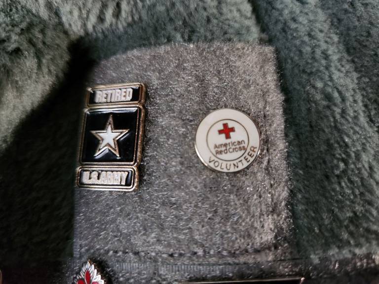A close up on Spc. Rose's flannel to show a set of pins attached near the chest. It's a "Retired U.S. Army" and "Red Cross Volunteer" pin