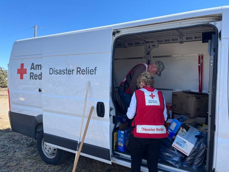 un hombre y una mujer con chalecos de la Cruz Roja Americana se preparan para distribuir suministros de asistencia.