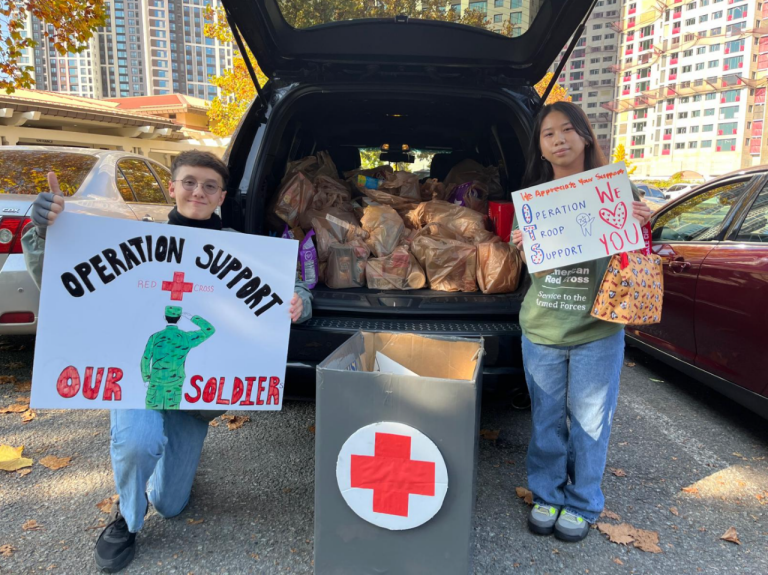  Dos jóvenes voluntarios de la Cruz Roja Americana están de pie con rótulos con el logotipo que dicen «Operation Support our Soldier», frente a una camioneta cargada de paquetes de apoyo.