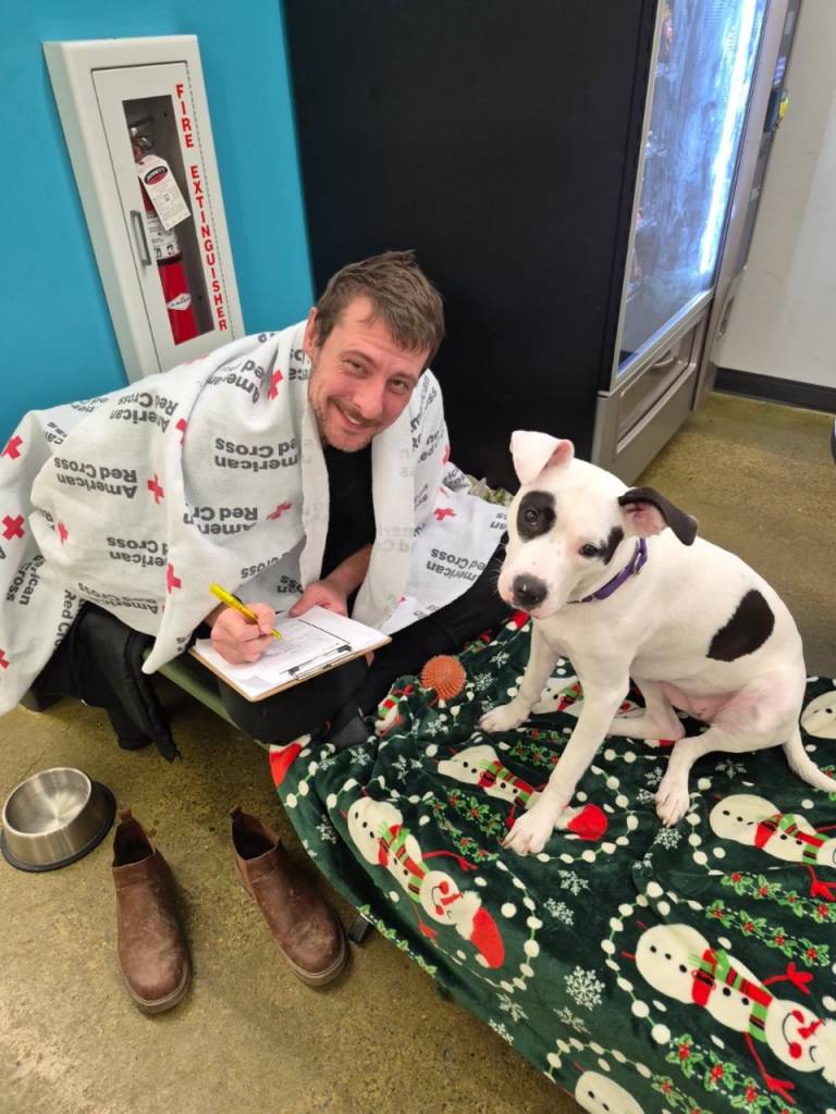 man and dog on a cot in a shelter