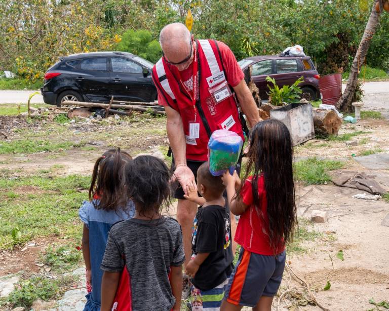 Man in Red Cross vest stands surrounded by children