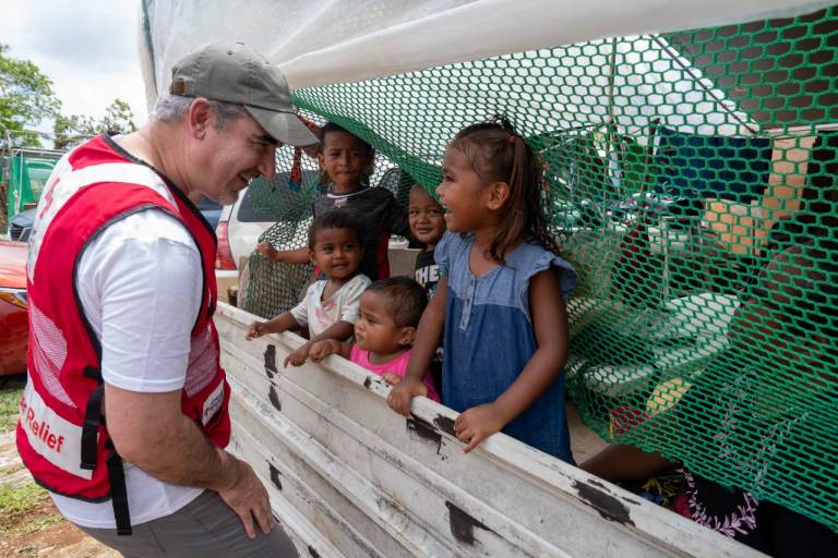 Man in Red Cross vest entertains several children