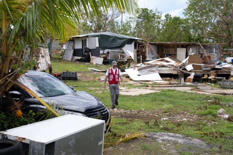 Man in Red Cross vest walks between damaged structures