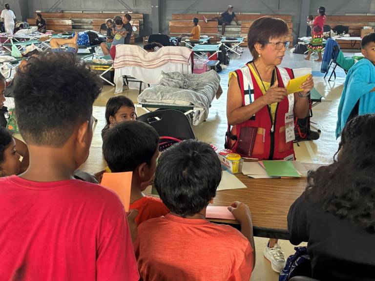 woman in red cross vest entertains children in shelter