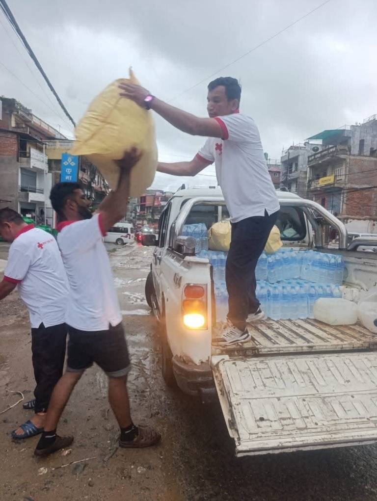 Three men in white t-shirts unload water and supplies from the bed of a truck.  
