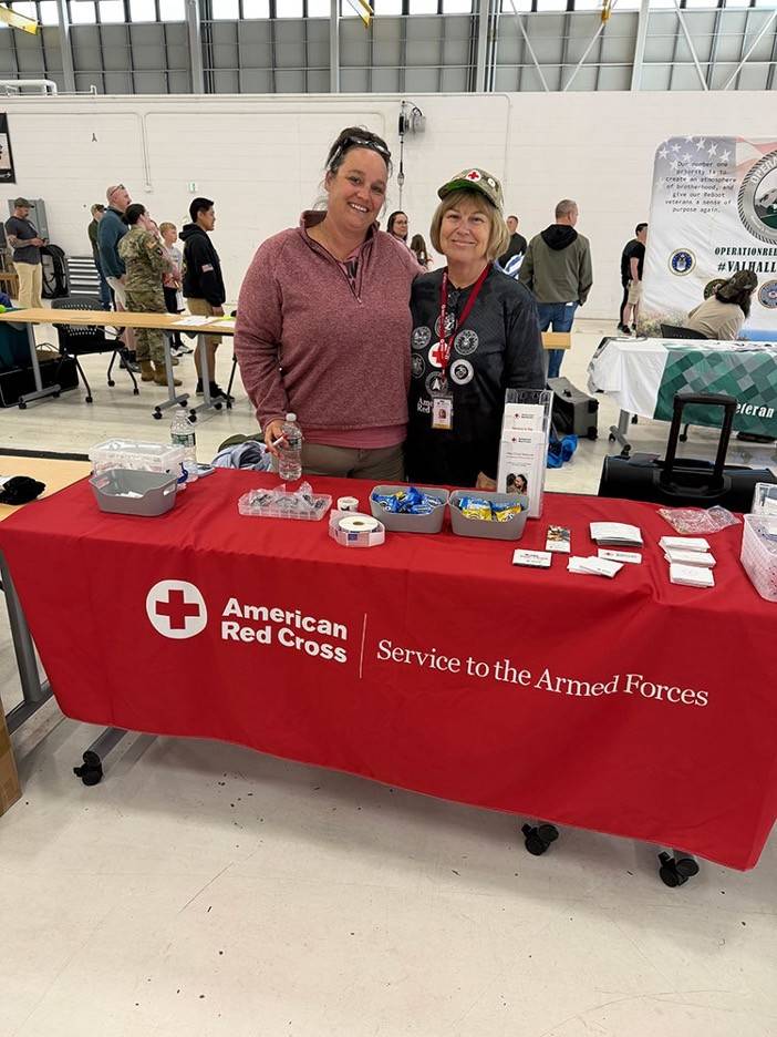 Two women stand together smiling wearing Red Cross clothing 