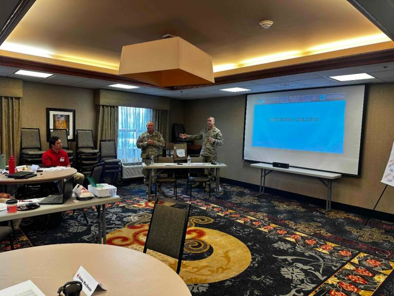 Two military members instruct a group of Red Cross staff before they deploy to military installations across the globe