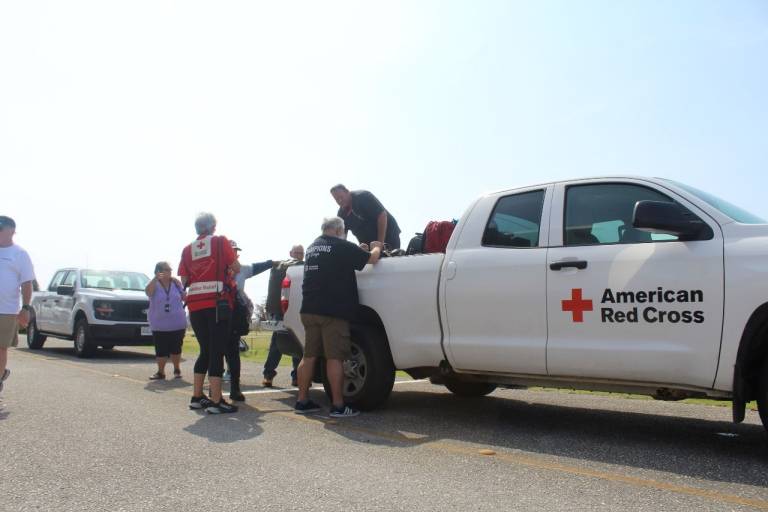 Volunteers, some in Red Cross shirts, remove equipment from Red Cross vehicle.