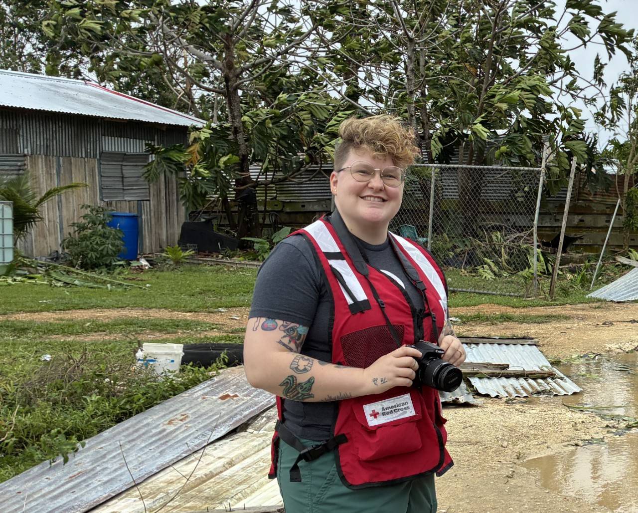 Woman in Red Cross vest stands in a street with her camera.