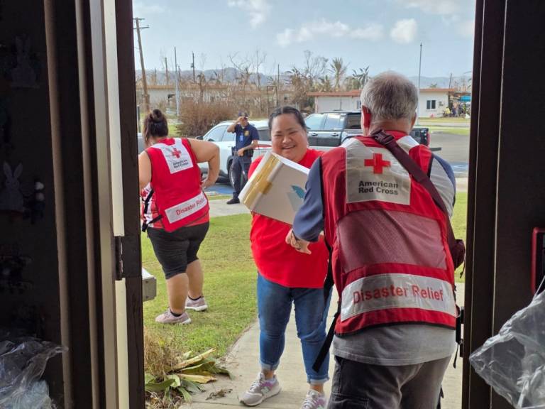 Volunteers in Red Cross vests deliver supplies to a shelter