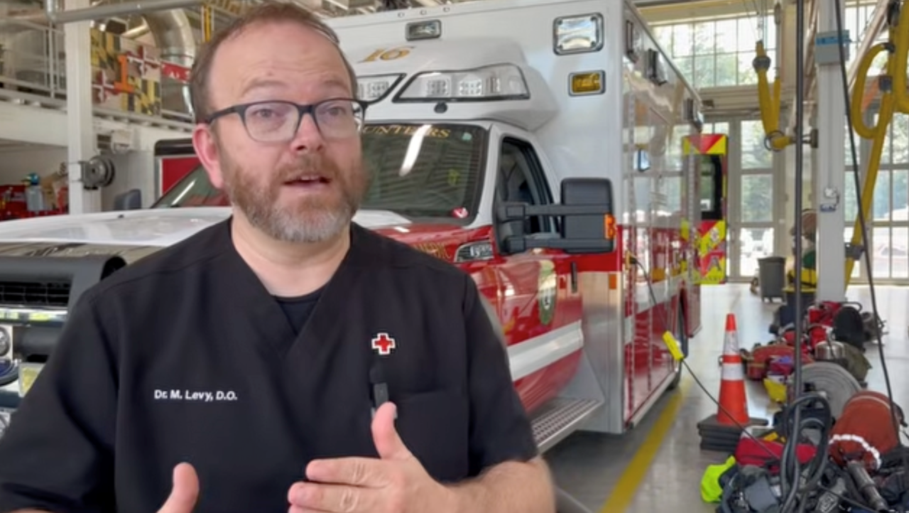 Photo of a man in black tee shirt with Red Cross pin.